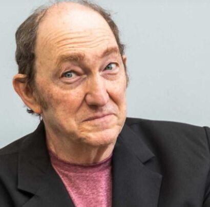 Adrián Stoppelman durante una emisión radial en estudio, con micrófono y auriculares, en plena editorial humorística.